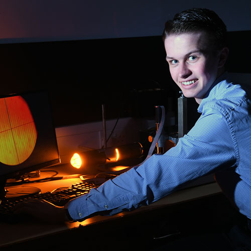 Physics with Teaching student Sam Templeton smiles at the camera while working at a computer in a physics laboratory Physics with Teaching student Sam Templeton smiles at the camera while working at a computer in a physics laboratory